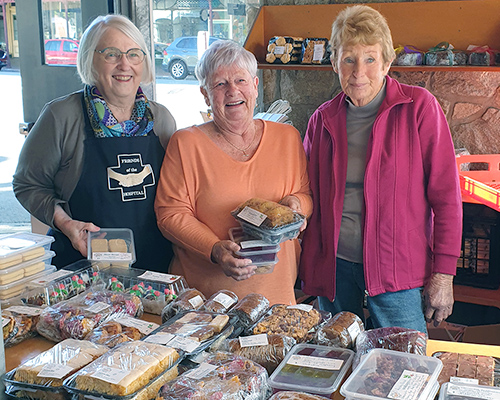 Three ladies from Friends of the Hospital Christmas Cake stall holding some cakes ready to sell.