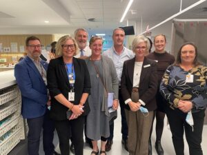 A group of eight adults, medical professionals and a member of Parliament standing in the middle of an emergency department. All are smiling. 