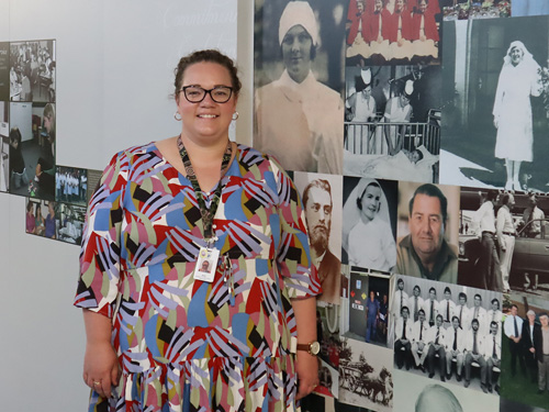 Jess Widdop standing in front of the wall covered in photos honouring nurses through the years at NHW.