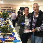 A couple stood next to a long table covered with cakes, slices and treats for Australia's Biggest Morning Tea