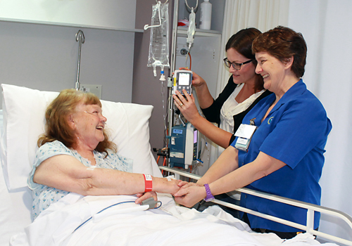 Two female nurses stood next to the bed of a smiling female patient